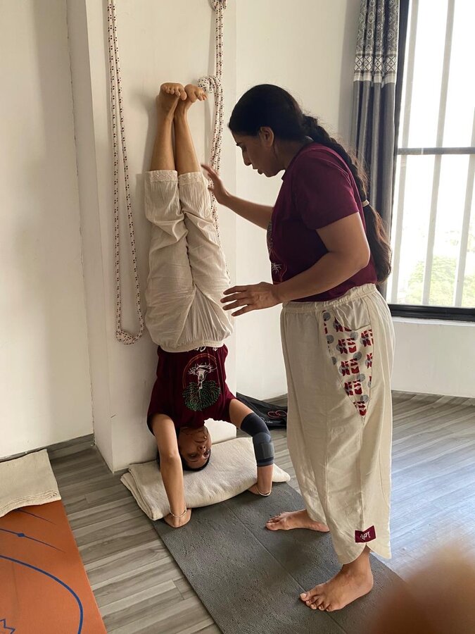 Instructor assisting a student into a supported headstand using traditional Iyengar ropes at YogStudio Kharghar